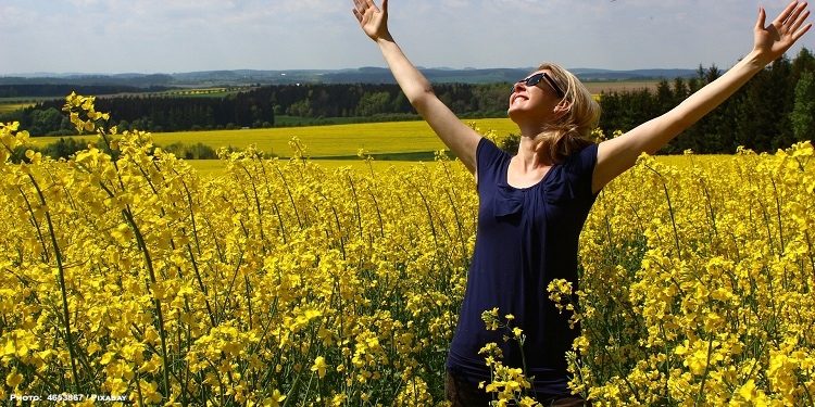 Young woman with her hands up rejoicing in a flower field.