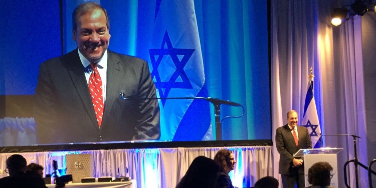 Rabbi Eckstein standing at a podium receiving a special award given to him and Mrs. Eckstein from a Women's group.