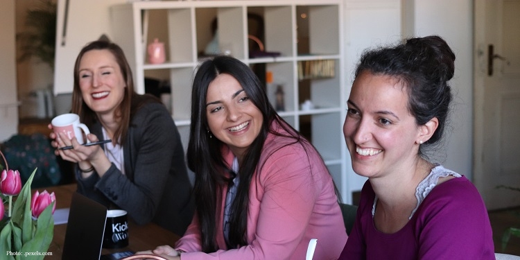 Three young women sit side by side laughing