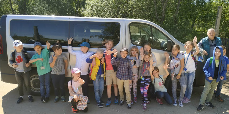 Second grade students in front of a silver van with their teacher.