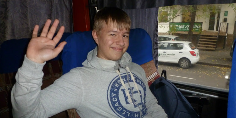 Young boy waving at the camera while sitting on the bus.
