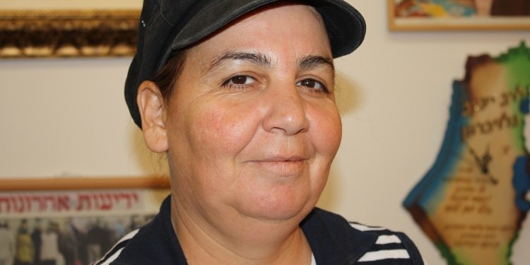 Middle aged woman in a black hat soft smiling at the camera.