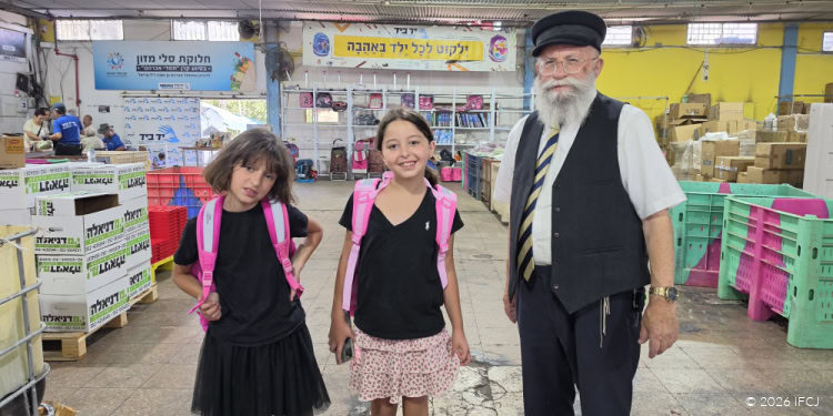 Smiling children with backpacks and an elderly man in a market setting, surrounded by colorful goods and shelves, representing community support and charity activities.