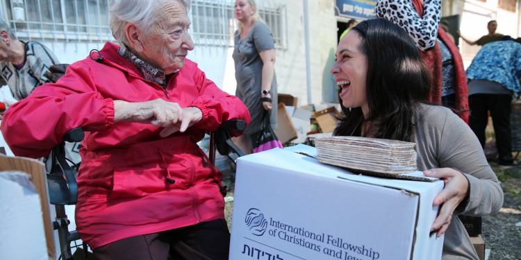 Yael Eckstein holding an IFCJ branded food box while talking to an elderly Jewish woman.