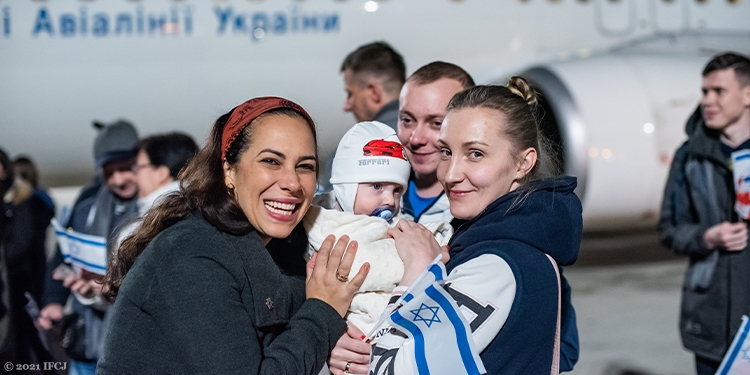 Yael Eckstein smiling next to a mother and her baby who just made aliyah.