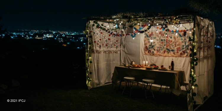 A lit sukkah with lights from the city behind it.