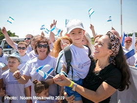 Yael holding a small smiling boy while others in the background are holding Israeli flags.