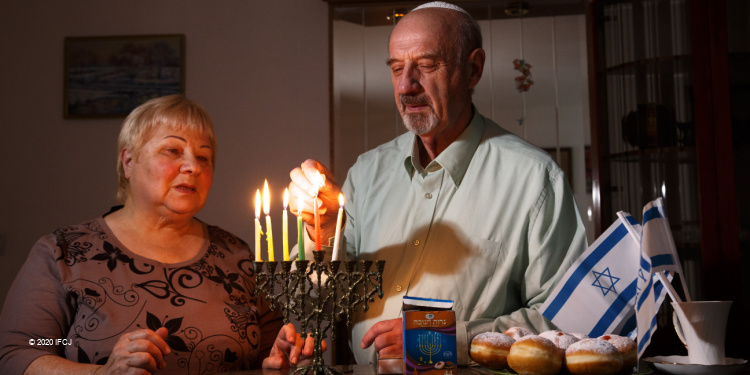 Elderly Jewish couple lighting menorah together on Hanukkah