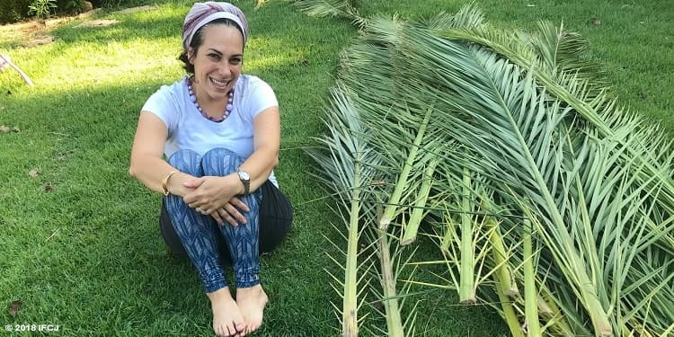 Yael Eckstein sits next to a pile of palm fronds for her sukkah