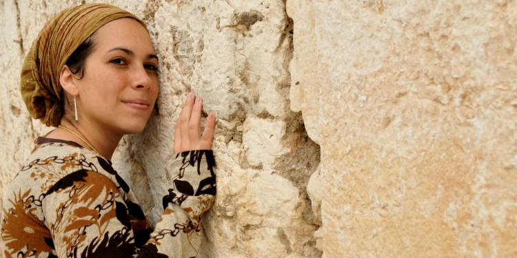 Yael Eckstein in a headscarf and brown patterned sweater leaning against the Western Wall.