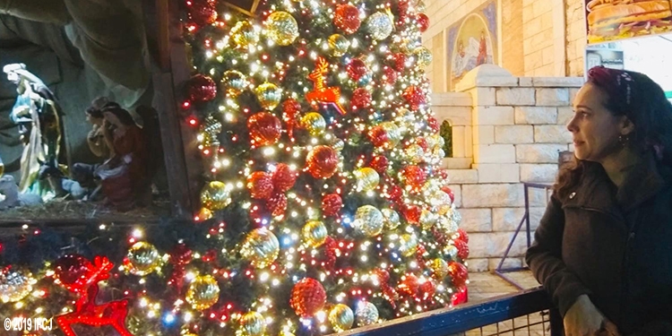 Yael Eckstein looking at a lit tree next to the Nativity scene.