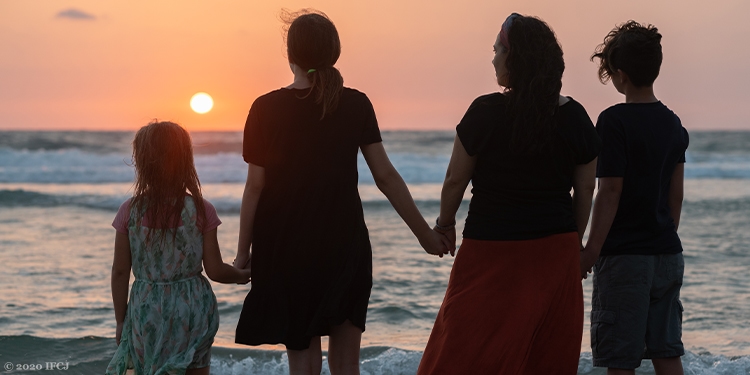 Yael holding hands with her children while looking at the sunset.