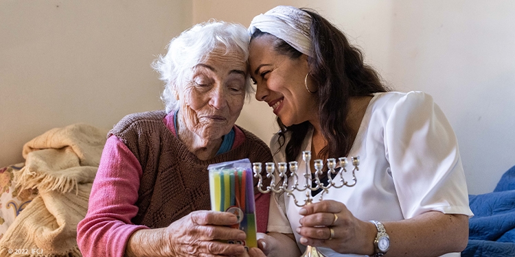 Yael and elderly woman holding a menorah.