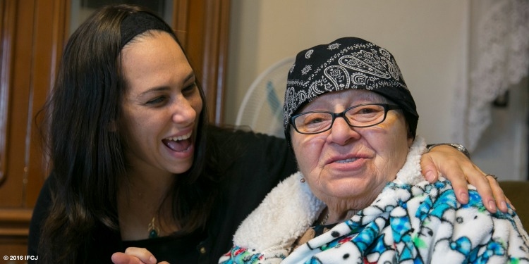 Yael Eckstein smiling at an elderly woman in a bandana and fuzzy sweatshirt looking ahead.