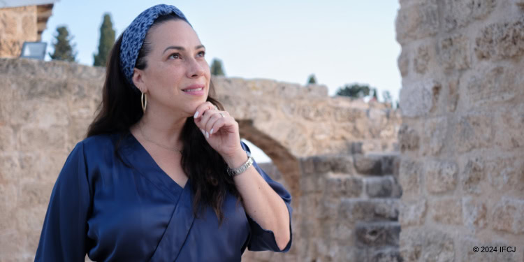 Yael Eckstein at Be'er Antilia, Israel in a navy blue satin dress with chin in hand looking thoughtful, pensive.