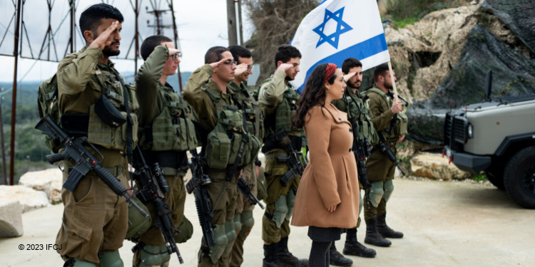 Yael Eckstein standing with several saluting IDF soldiers who are also holding the Israeli flag.