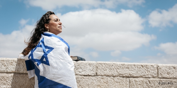 Yael looking upward at the Western wall wearing the Israeli flag.