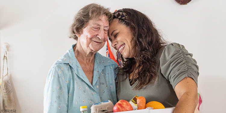 Yael joyfully smiling with elderly woman holding a food box