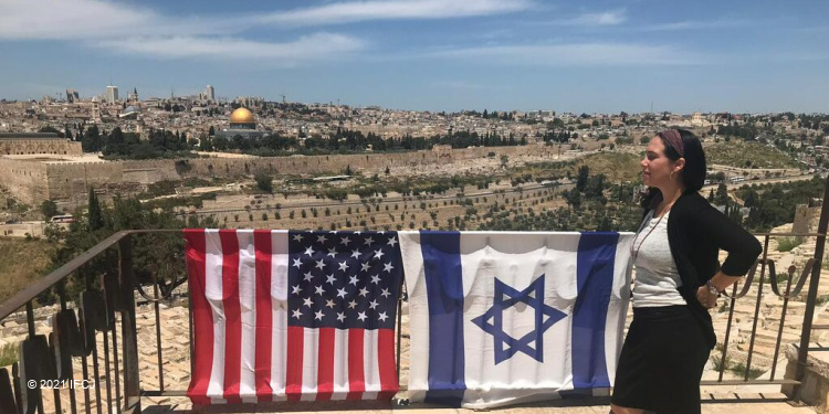 Yael Eckstein standing on a platform with the Israeli and American flags draped over the railing.