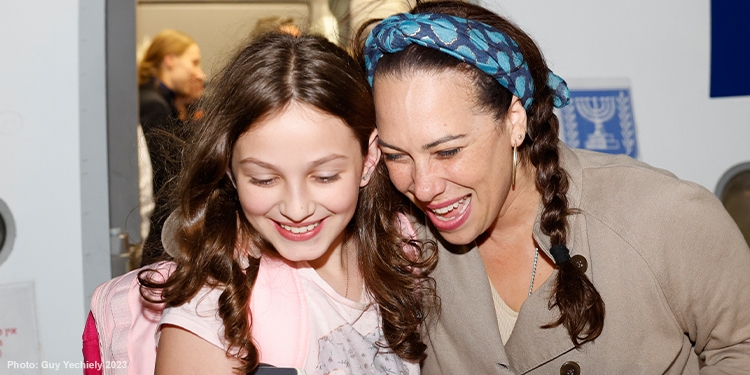 Yael smiling with a young girl as they exit a plane from an Aliyah flight.