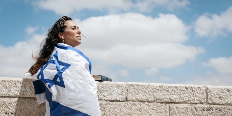 Yael looking to her right while having the Israeli flag draped around her.