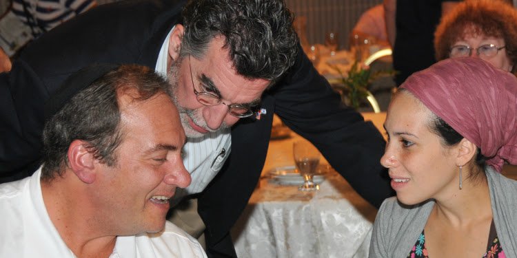 Rabbi and Yael Eckstein at a dinner talking with a man.