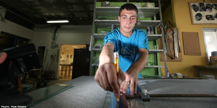 A young man measuring out a piece of glass in a wood working shop.