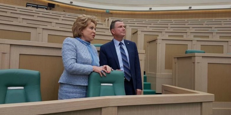 A man and woman both in suits standing in an empty lecture auditorium.