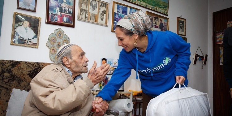 Yael Eckstein in an IFCJ branded sweatshirt delivering a blanket to an elderly Jewish man.