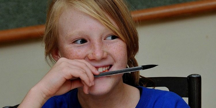 Young girl biting her pencil while smiling.