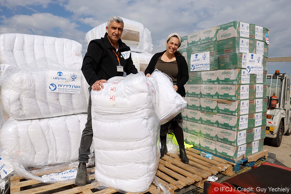 Yael Eckstein standing with a man next to humanitarian aid packages.