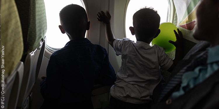 Two young children looking out the window on the plane of an aliyah flight.