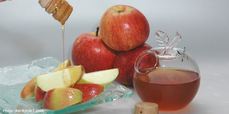 Three apples stacked on top of each other with a plate of cut apples and honey drizzled on top of it.