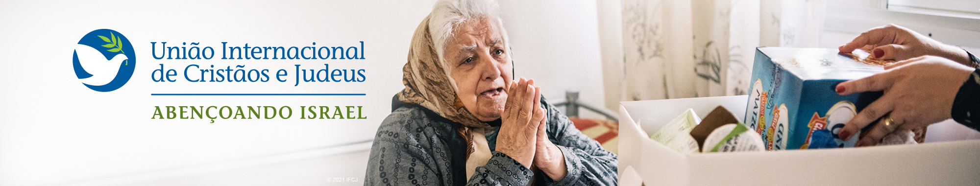 Elderly woman with her hands in prayer as an IFCJ food box is approaching her.