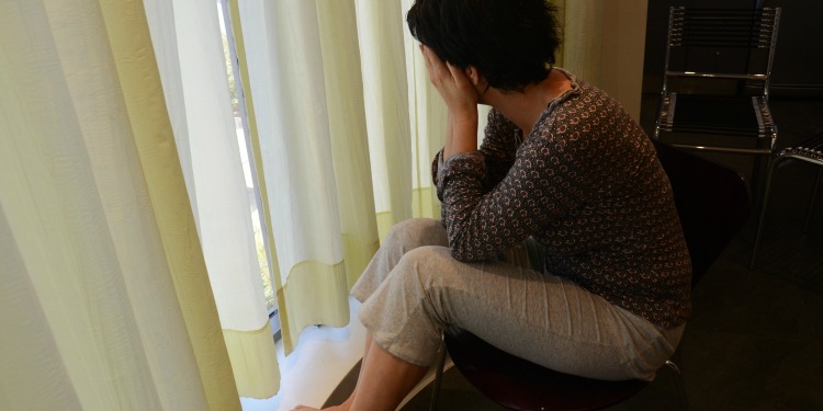 A woman with her hands over her face looking out the window.