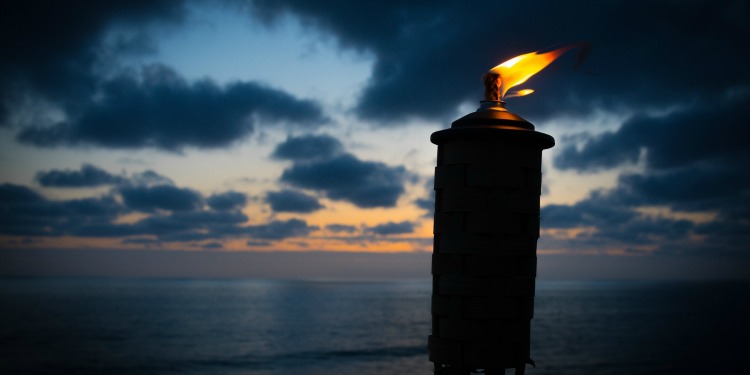 A lantern lit next to a body of water as dusk is setting in.