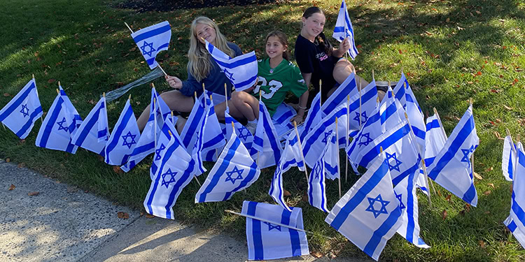 Group of children sitting on grass surrounded by Israeli flags, celebrating with smiles and patriotic spirit.