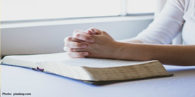 Hands folded over an open Bible.