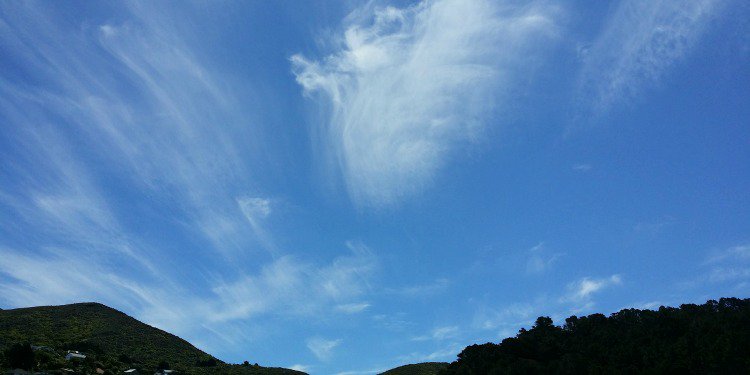 Blue skies with trees and hills below it.