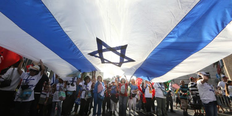 Several people marching in the street while holding an Israeli flag above their heads.