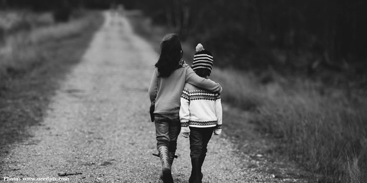 Black and white image of a young boy and girl walking on a dirt road.
