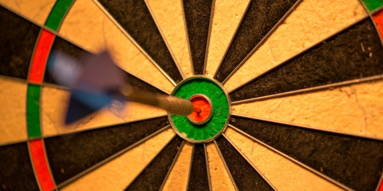 A dart right in the center of the bulls eye in a dart board.