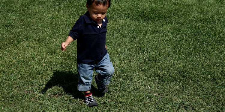 Young boy running through a patch of grass.