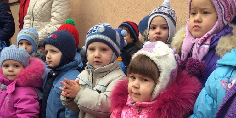 Young children lined up while wearing winter jackets and hats.
