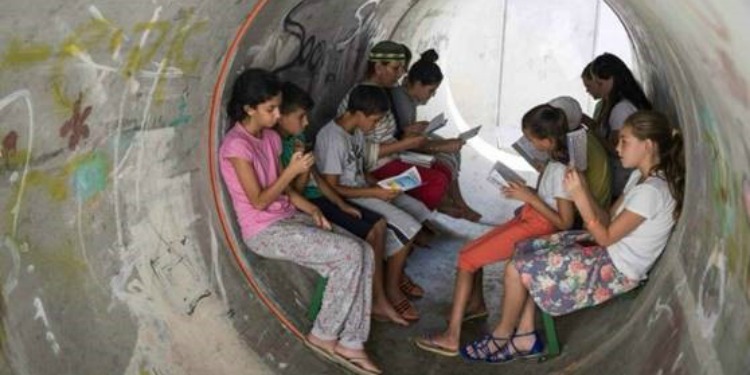 Several children reading small leaflet books as they sit inside a bomb shelter.