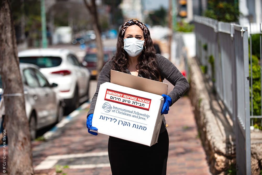 Yael Eckstein, wearing surgical face mask and gloves, walking down empty street distributing emergency package with food and cleaning supplies.