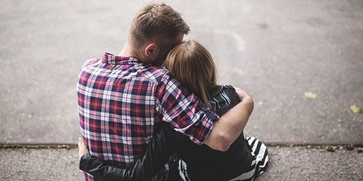 A couple embracing each other as they sit on the sidewalk.
