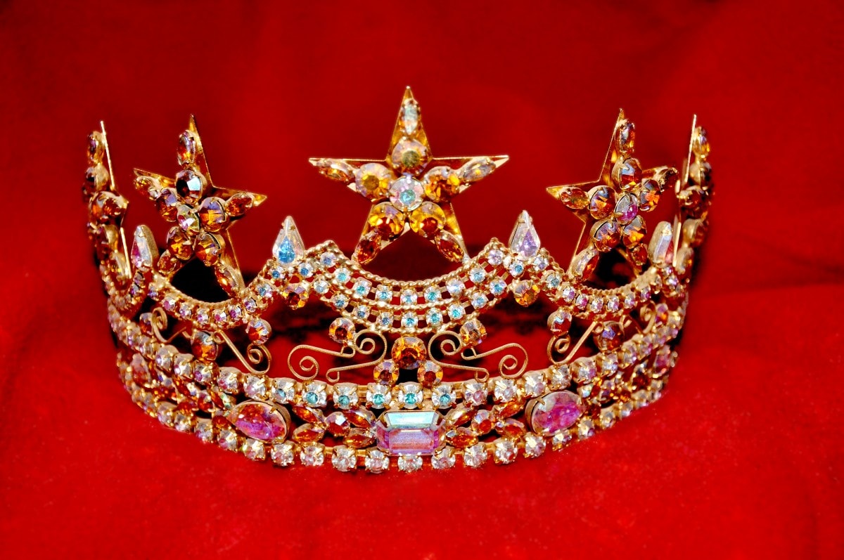 A bejeweled crown against a red background.