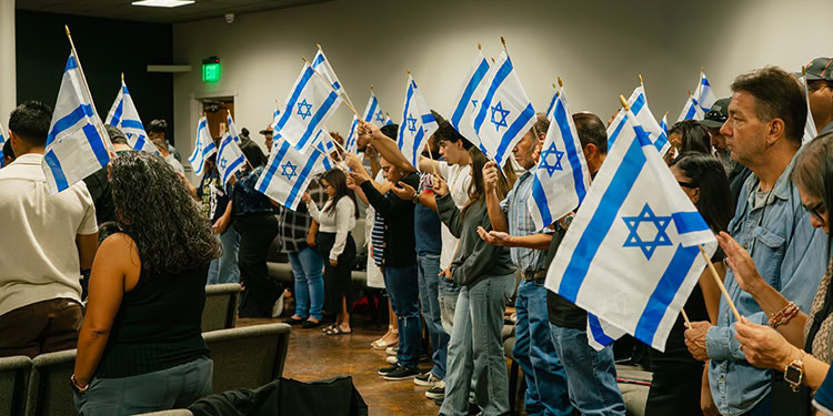 Group of people holding Israeli flags during a rally, demonstrating support and unity for Israel.