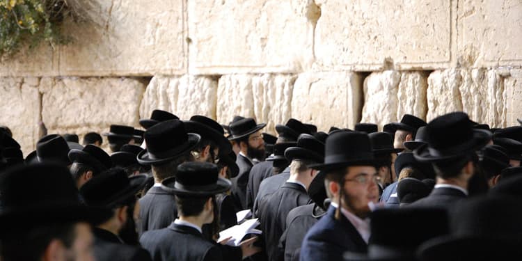 Men gathering at the Western Wall in black hats.